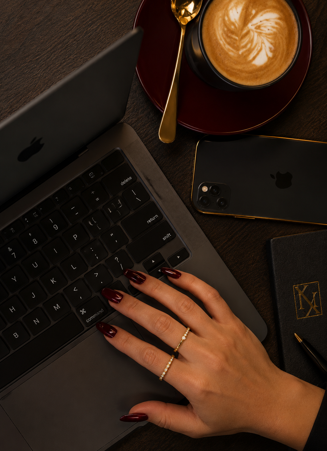 Woman's hands typing on laptop in office with coffee and iphone beside her.