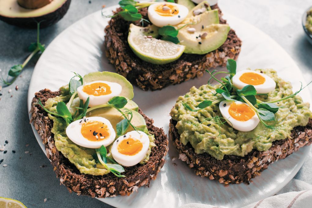 Post-Workout-Snack für Frauen aus der Perimenopause: Vollkornbrot mit Avocado-Creme und Ei auf weißem Teller