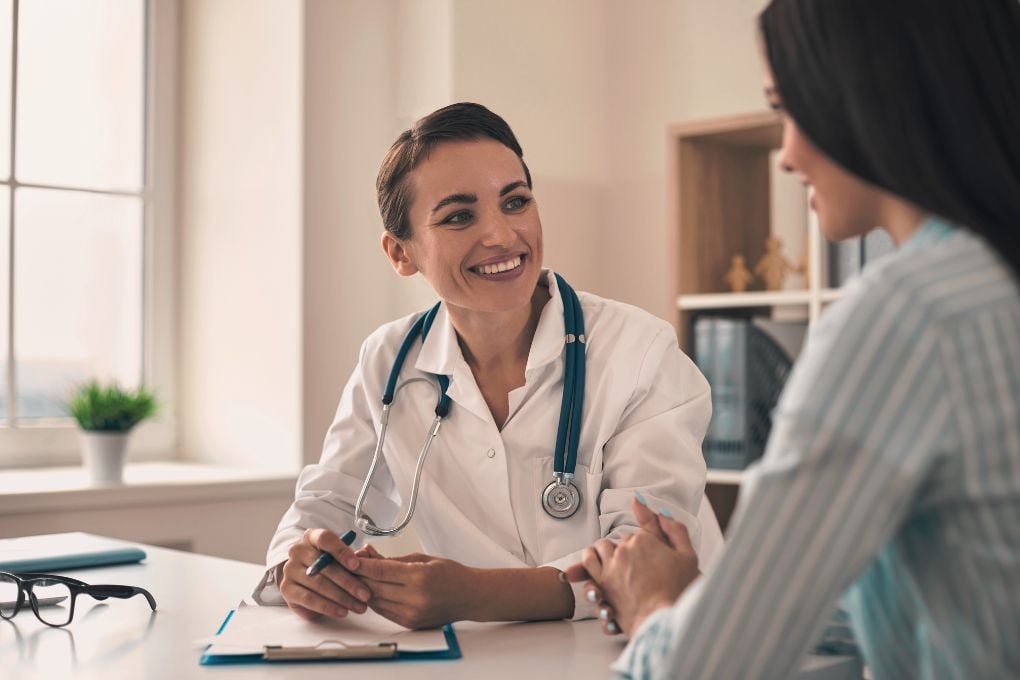 Eine Ärztin mit Stethoskop lächelt und spricht mit einer Patientin in einem Beratungszimmer, was auf eine vertrauensvolle Arzt-Patienten-Interaktion hinweist, möglicherweise im Kontext der Behandlung von Wechseljahresbeschwerden oder hormonellen Veränderungen.