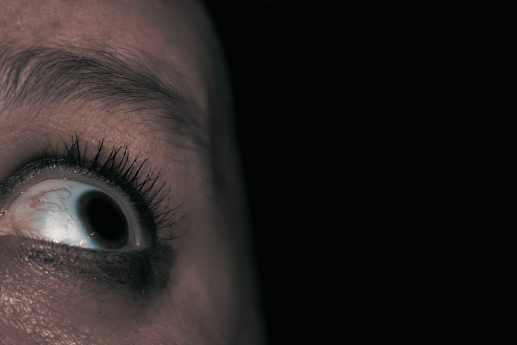 Nahaufnahme eines weit aufgerissenen Auges mit sichtbaren Äderchen, das Ausdruck von Angst, Panik oder innerer Unruhe zeigt, vor einem dunklen Hintergrund