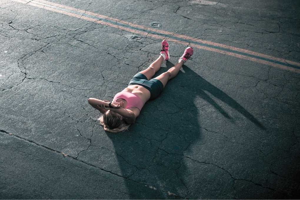 Erschöpfte Frau in Sportkleidung liegt auf dem Asphalt – Symbol für die Auswirkungen von Östrogenmangel auf Energie, Trainingseffektivität und Erholung in der Perimenopause.