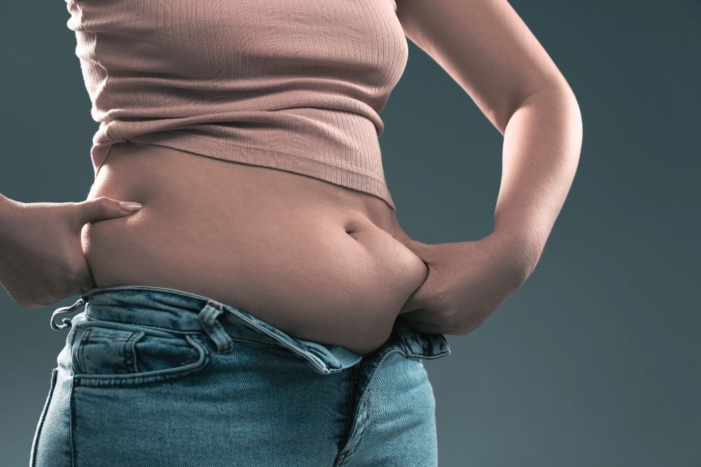 Frau hält Bauchfett fest – plötzliche Gewichtszunahme am Bauch als mögliches Symptom der hormonellen Umstellung in der Perimenopause.