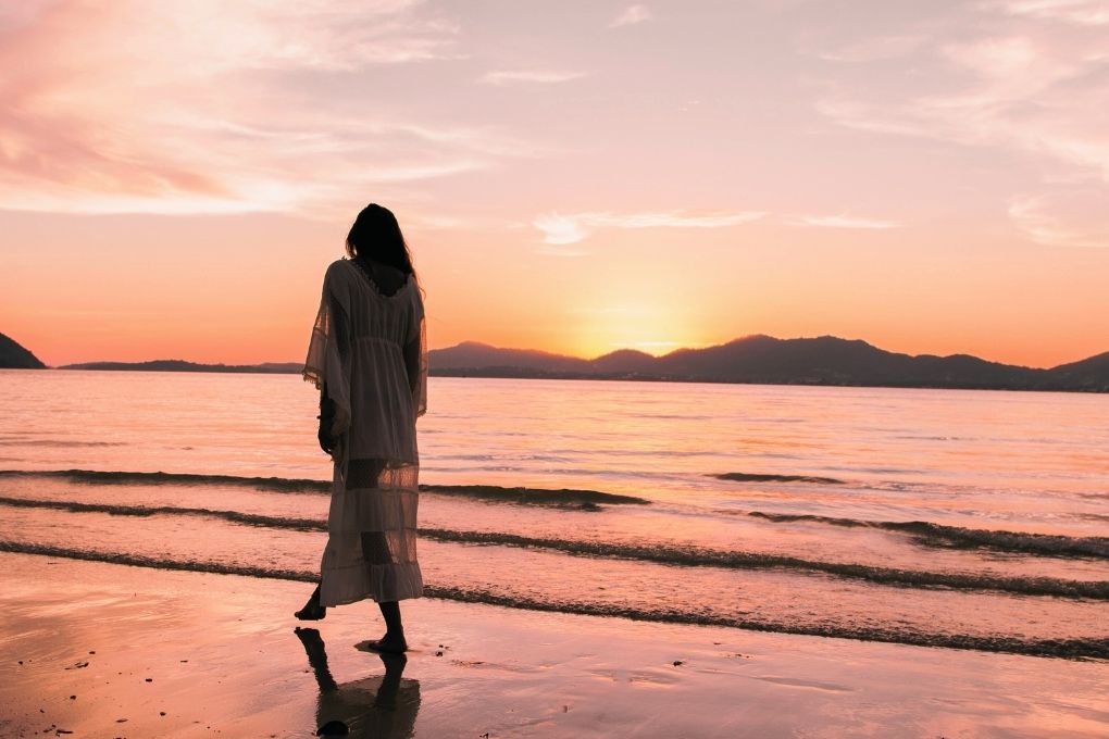 Frau in langem Kleid geht am Strand bei Sonnenuntergang – Symbol für Achtsamkeit, hormonelle Balance und den Umgang mit Veränderungen in der Perimenopause.