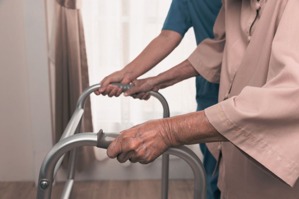 Nahaufnahme einer älteren Person, die mit einem Gehwagen unterstützt wird, begleitet von einer helfenden Hand. Dieses Bild symbolisiert die Folgen von Muskelschwund (Sarkopenie) im Alter, eine mögliche Auswirkung hormoneller Veränderungen wie in den Wechseljahren