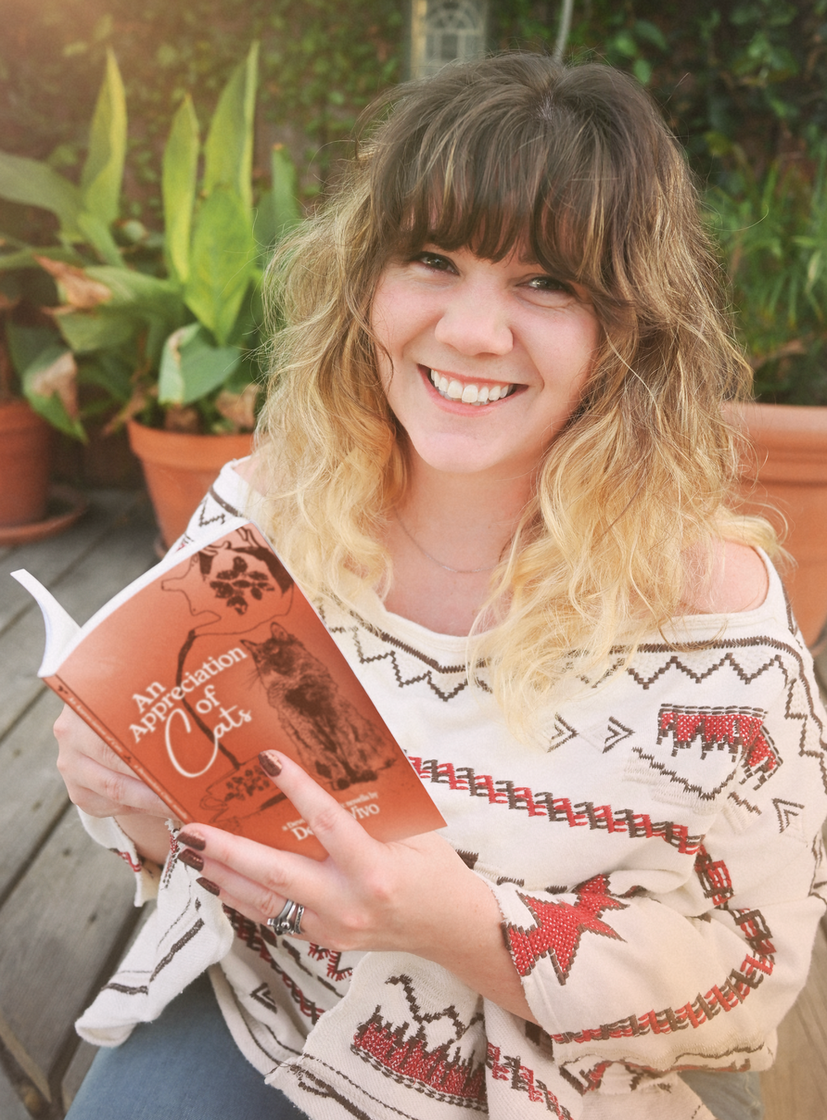 Smiling white person sitting on a deck holding an open book. Author photo of Des DeVivo