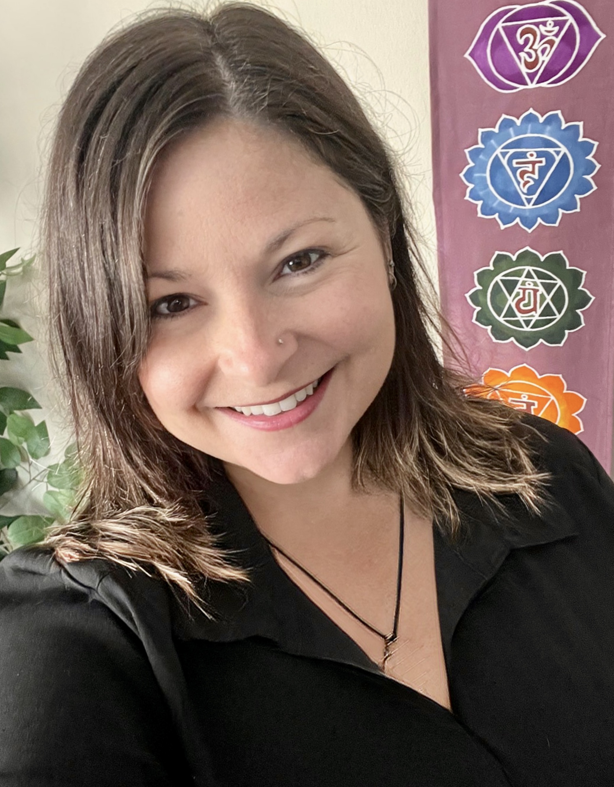Lana, Certified Crystal and Reiki Practioner, SharQui Bellydance Instructor, and Sistership Circle Facilitator of Winnipeg, MB,  stands in front of a Chakra Flag and smiles with welcome