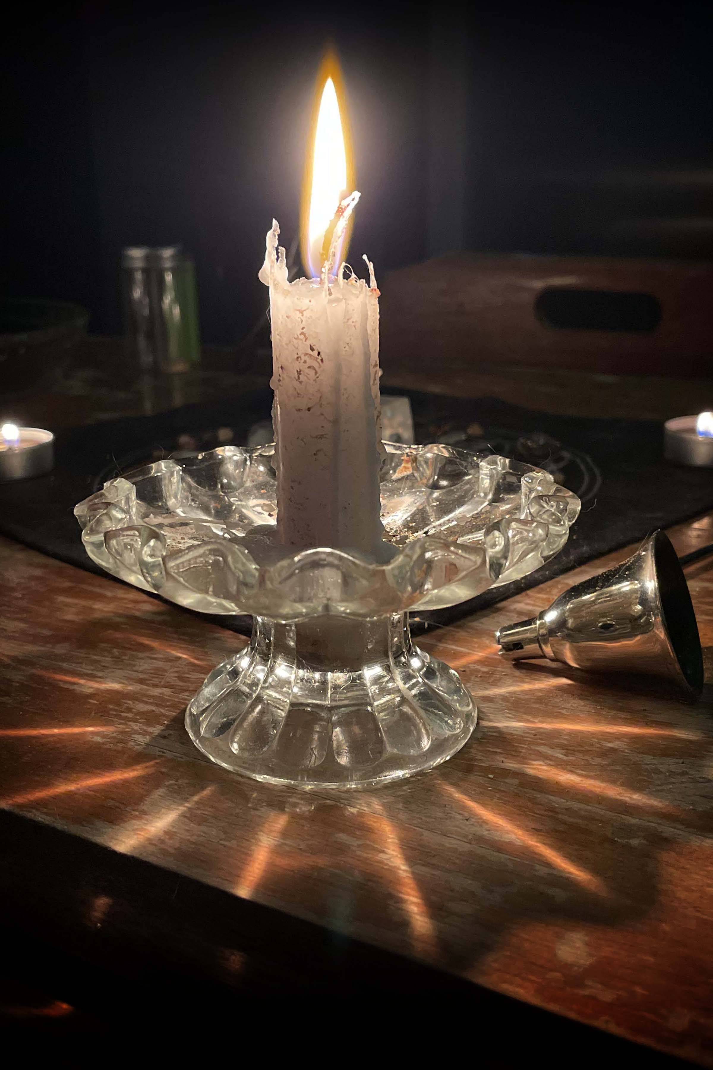 A single white candle glows in a darkened room, hiding the crystal grid behind it.
