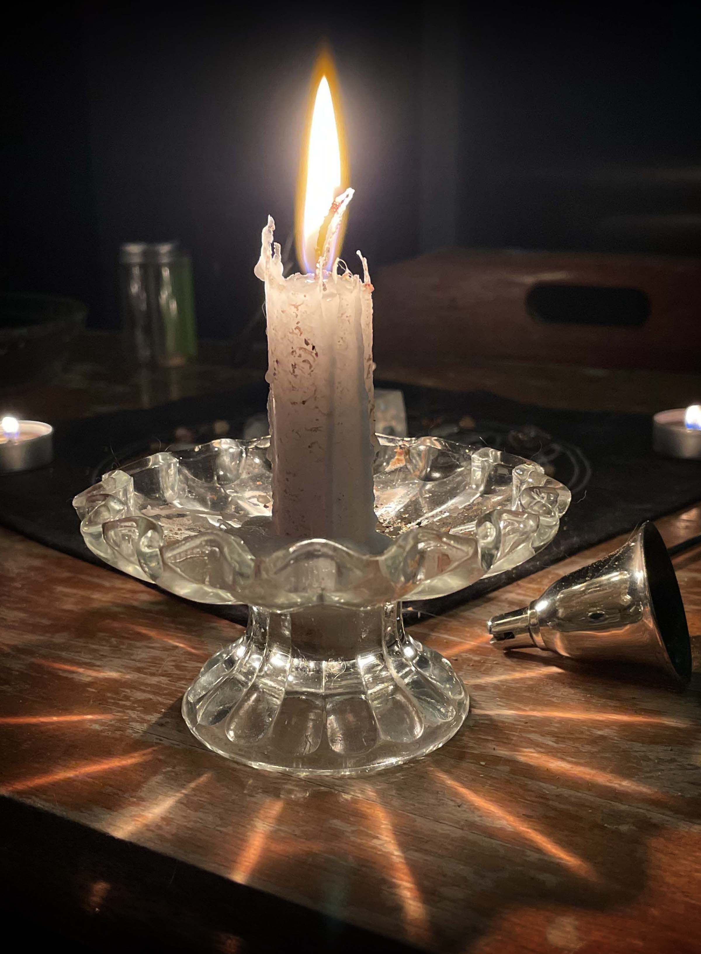 A single white candle glows in a darkened room, hiding the crystal grid behind it.