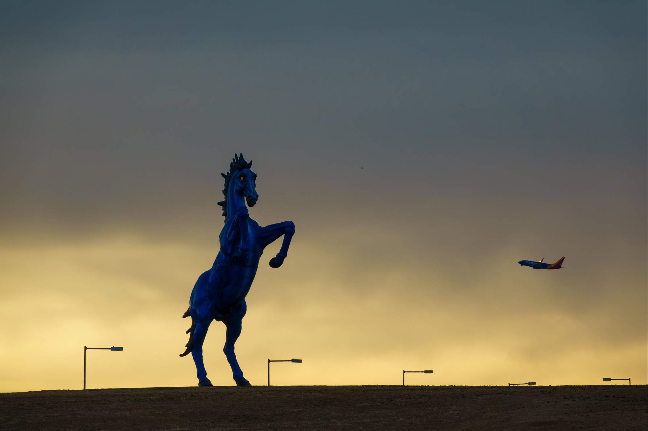 tall statue of bucking blue horse with plane taking off in background