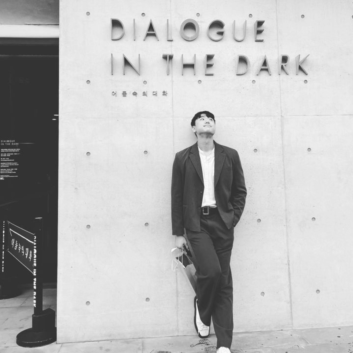 Foto of one person leaning on a wall in front of the dialogue in the dark sign in Seoul.